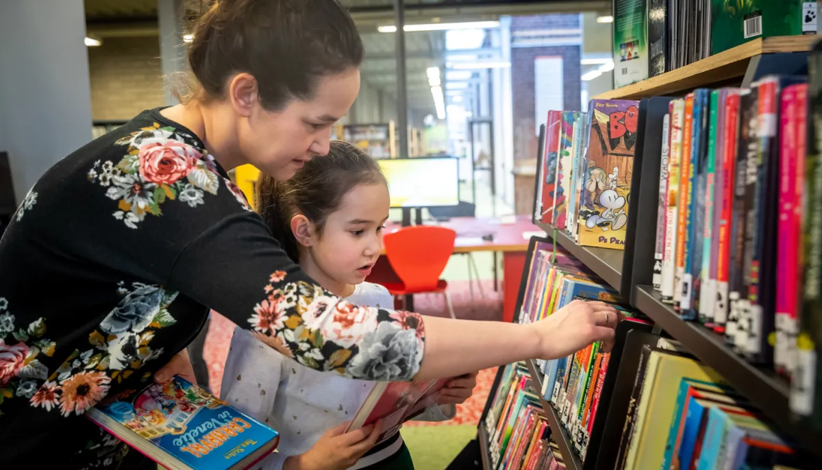 Moeder en kind zoeken boeken in kast 