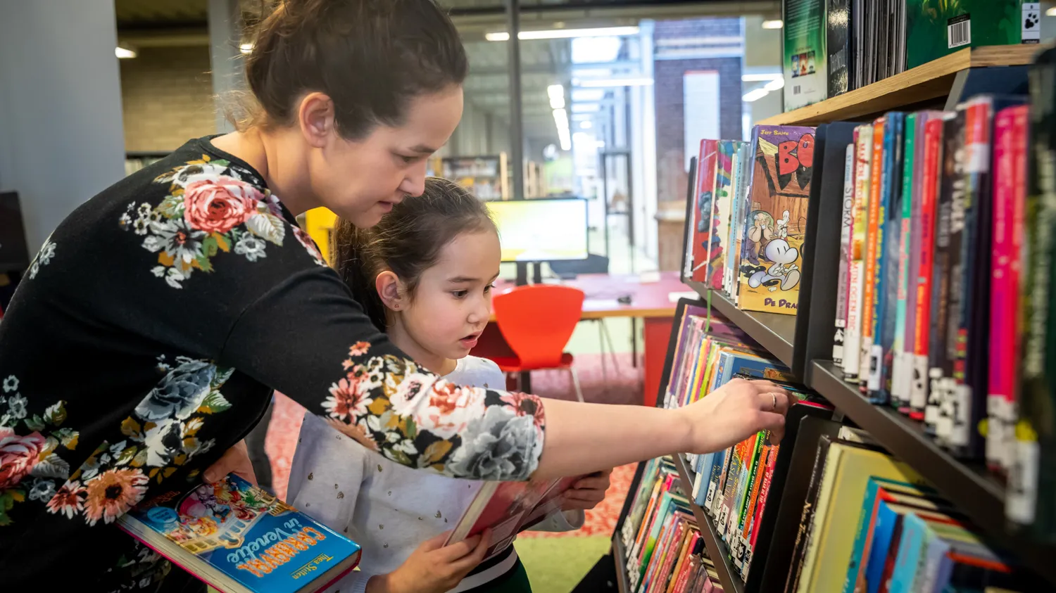Moeder en kind zoeken boeken in kast 