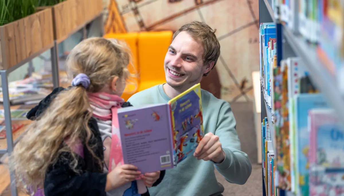 Lachende man en meisje in schoolbieb met boek in hand