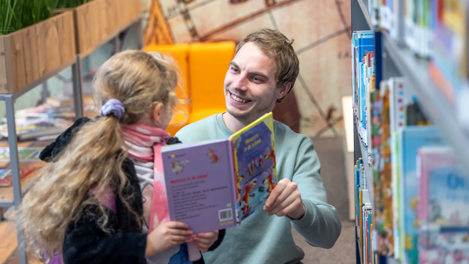 Lachende man en meisje in schoolbieb met boek in hand