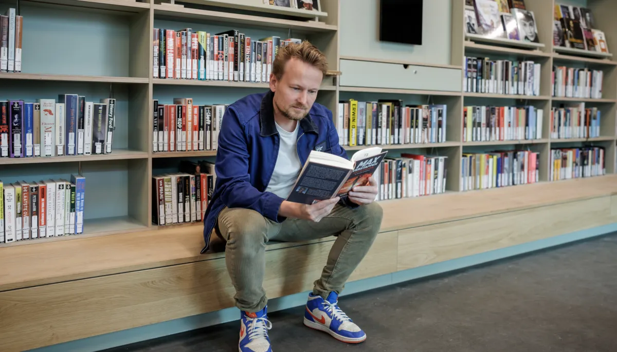 man lezend voor boekenkast