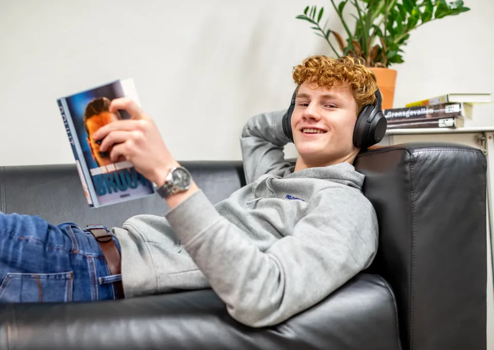 jonge man liggend op bank met koptelefoon en boek