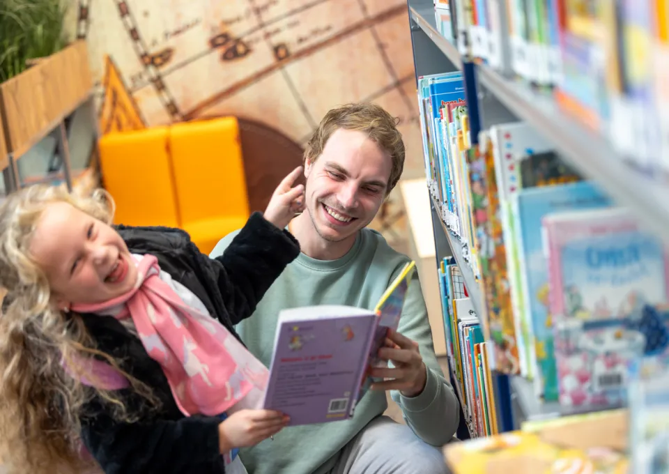 Lachende leerkracht en kind bij boekenkast