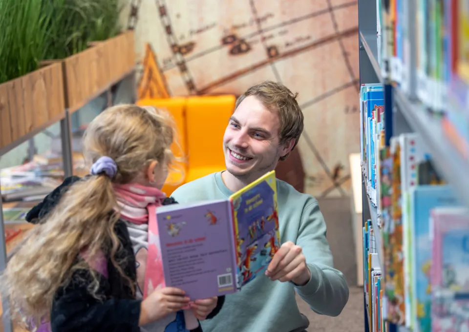 Lachende man en meisje in schoolbieb met boek in hand