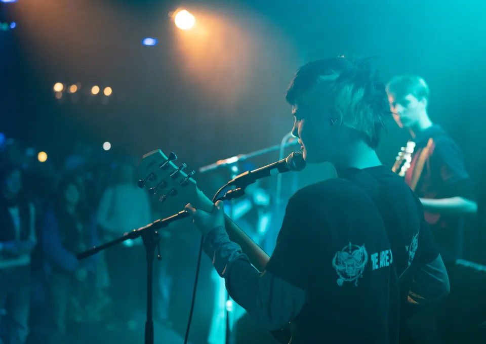 Twee rockende jongeren met gitaren voor een publiek in een poppdium rook en blauw licht 