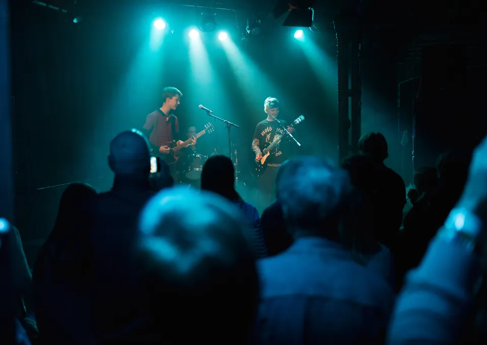 Volle zaal rock band groen blauw licht podium twee personen gitaren en zang