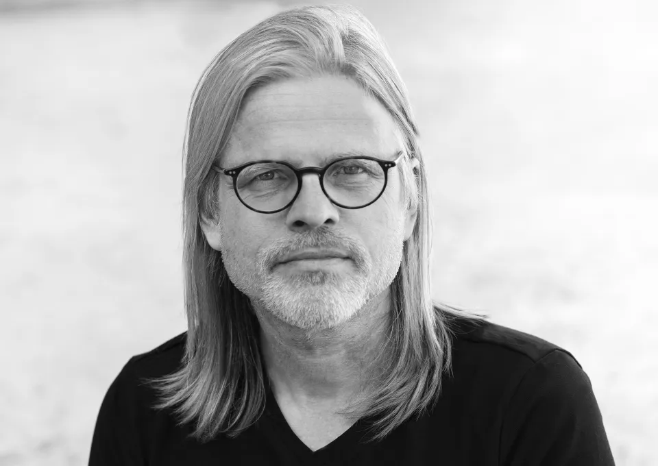 De schrijver is te zien: lang sluik haar, snor en bril. 