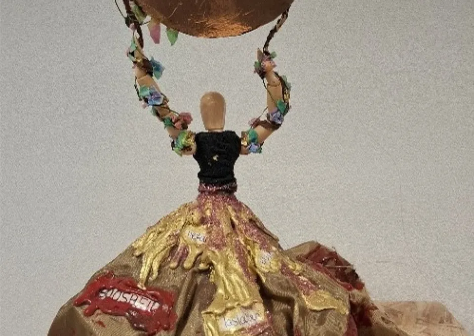 Kunstwerk van houten poppetje met stoffen jurk en koperkleurige cirkel