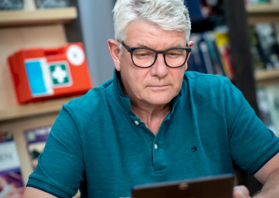 Man met grijs haar, bril en blauwe polo kijkt naar zijn tablet