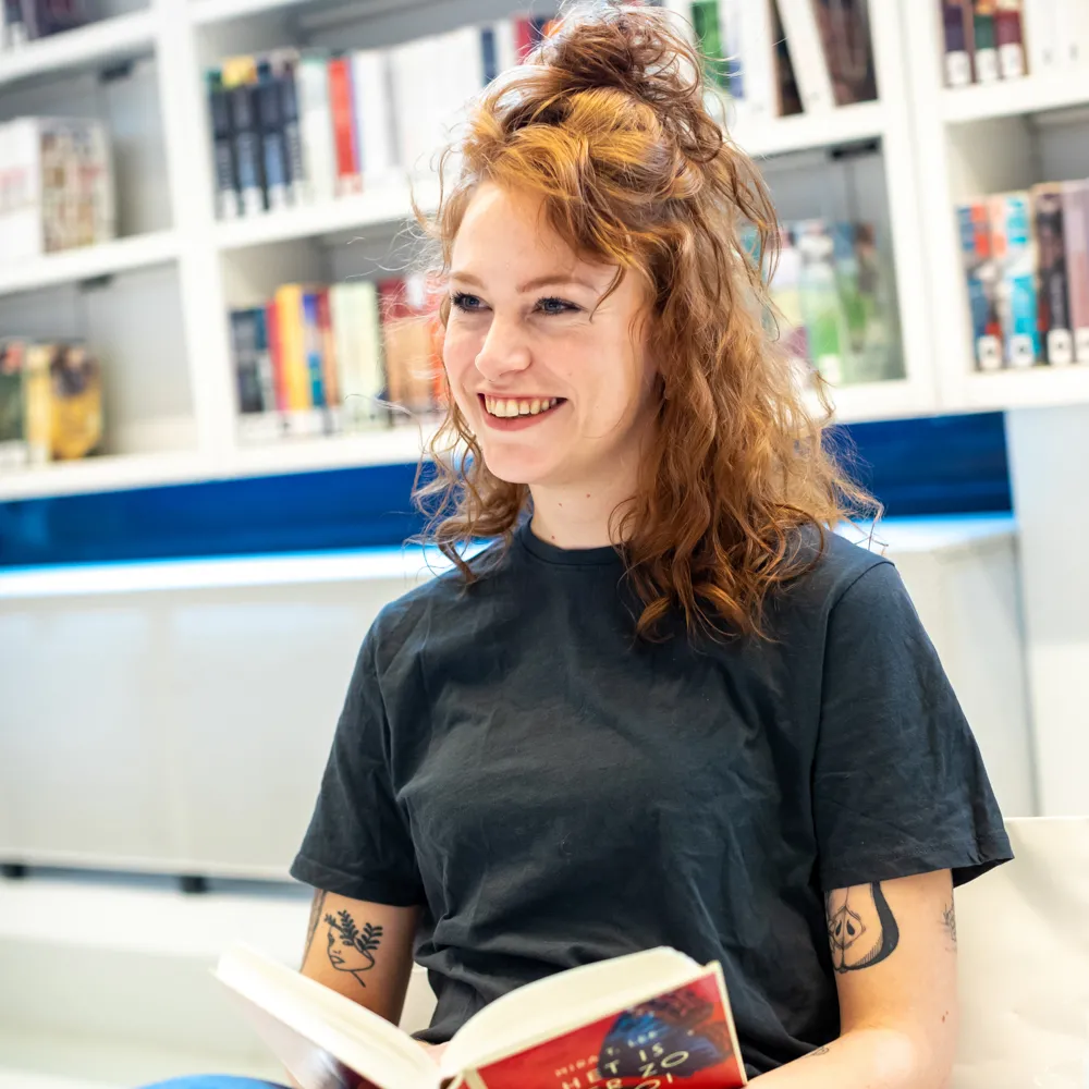 jonge vrouw met boek voor boekenkast boekenclub boekenbabbelaars