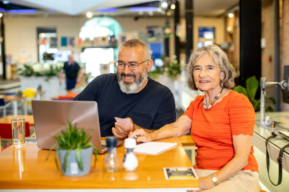 Een man en een vrouw zitten samen lachend achter een laptop.