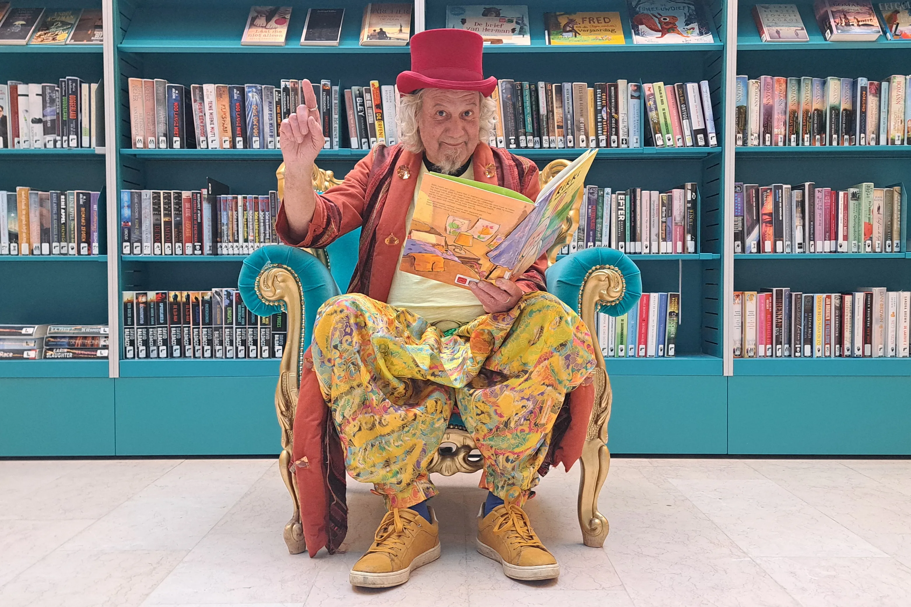 De verhalenverteller zit op een voorleesstoel in de bibliotheek van Sint-Michielsgestel in kleurrijke kleding