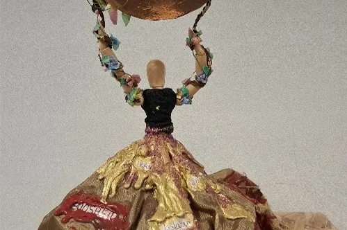 Kunstwerk van houten poppetje met stoffen jurk en koperkleurige cirkel