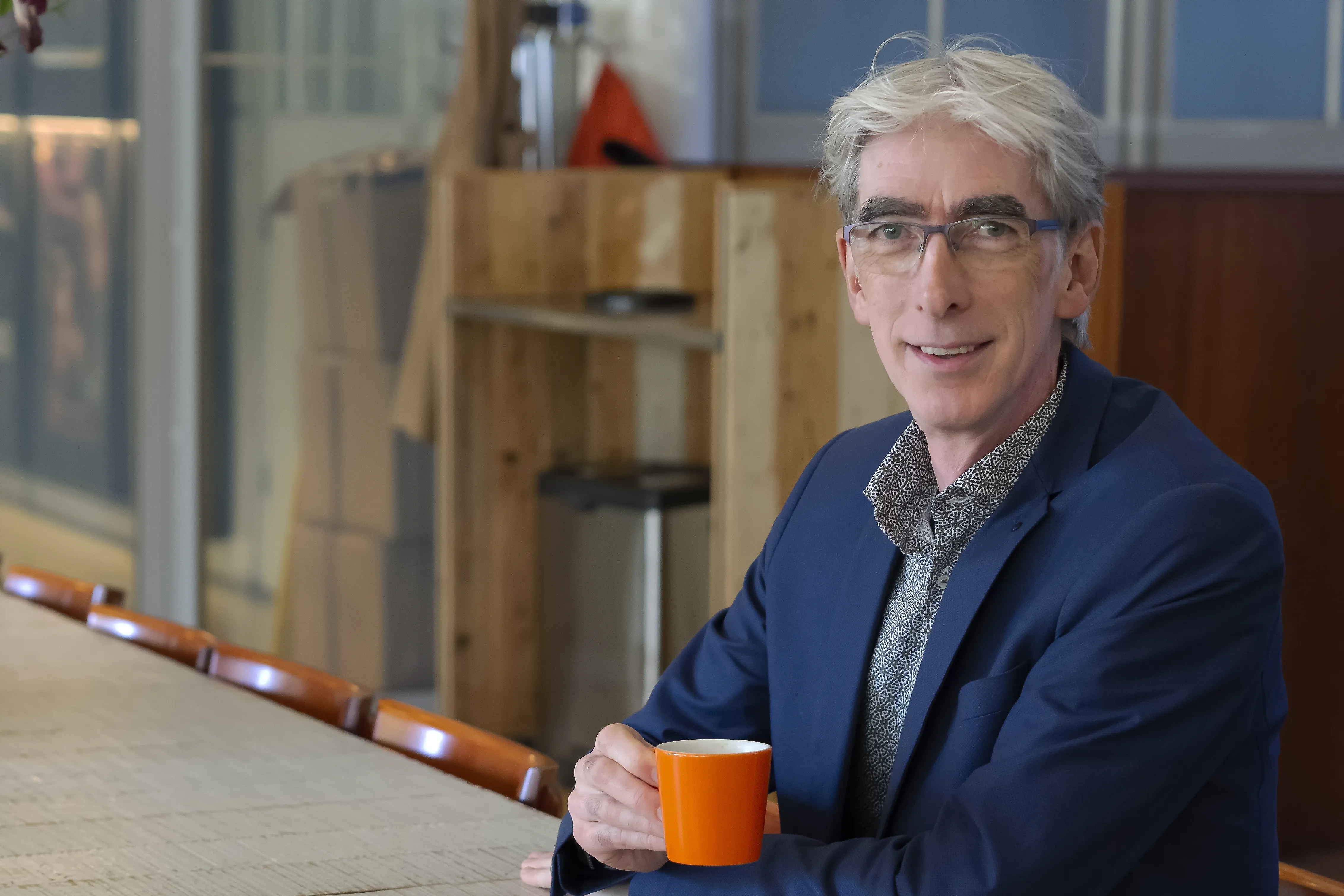 man met grijs haar en een bril met een kopje koffie
