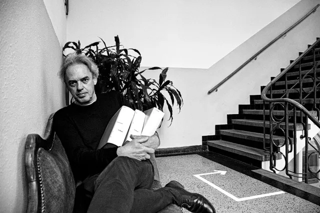 Zwart-wit foto van Eric Alink op stoel met achter hem een plant en een trap