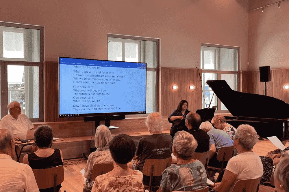Publiek in zaal met scherm en piano 