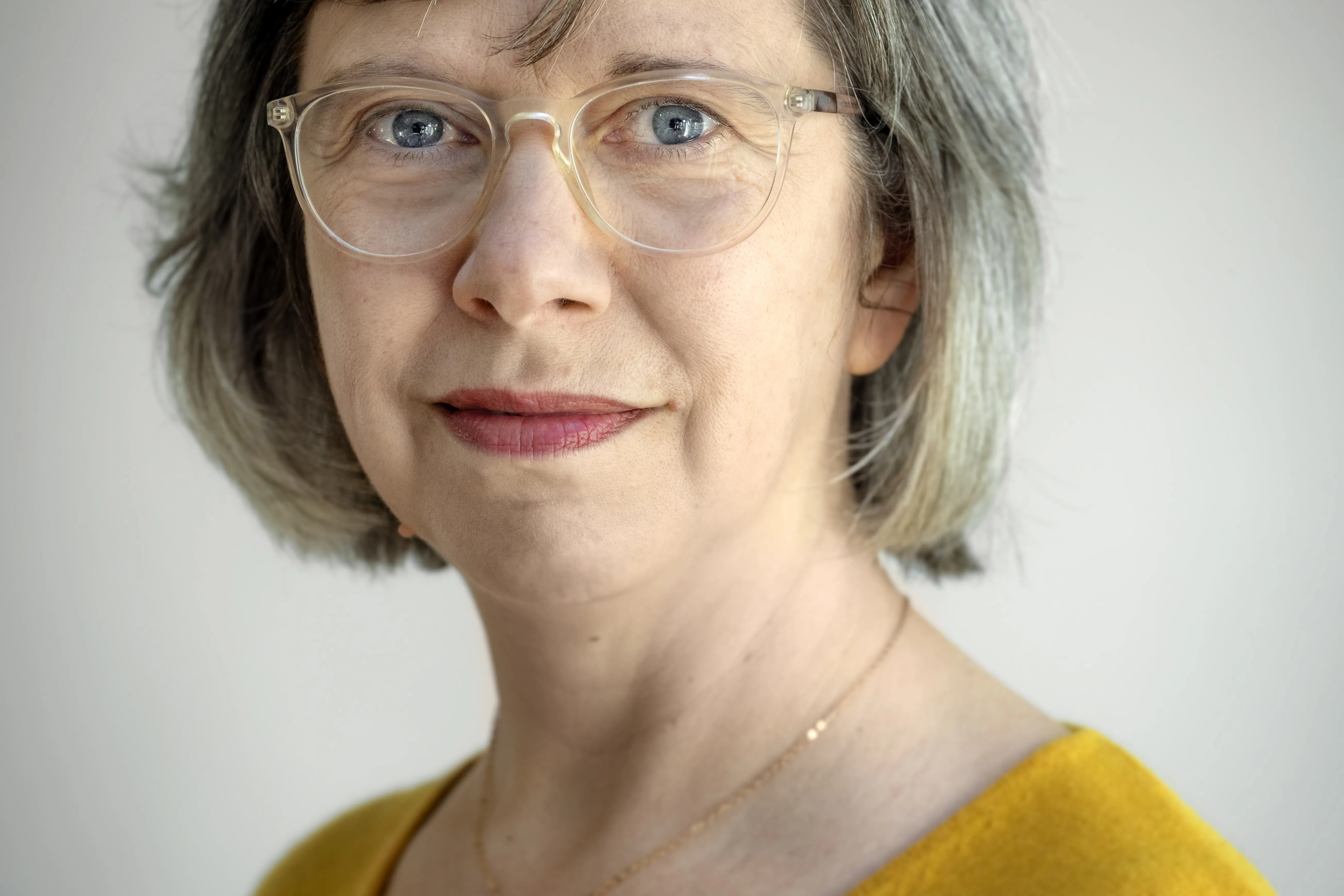 Portret van vrouw van middelbare leeftijd met grijze bob, bril en gele trui