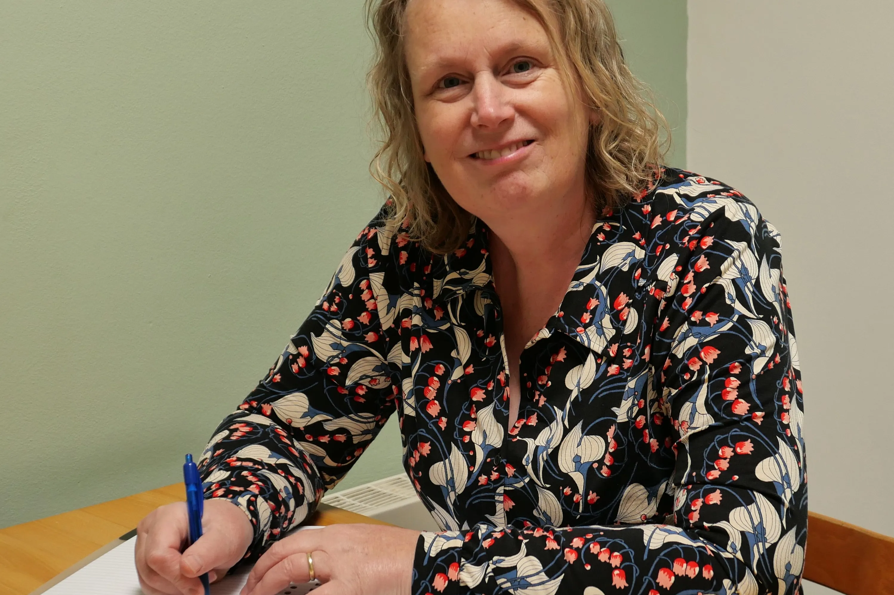 Foto vrouw met lichtbruin haar die achter een bureau zit en schrijft