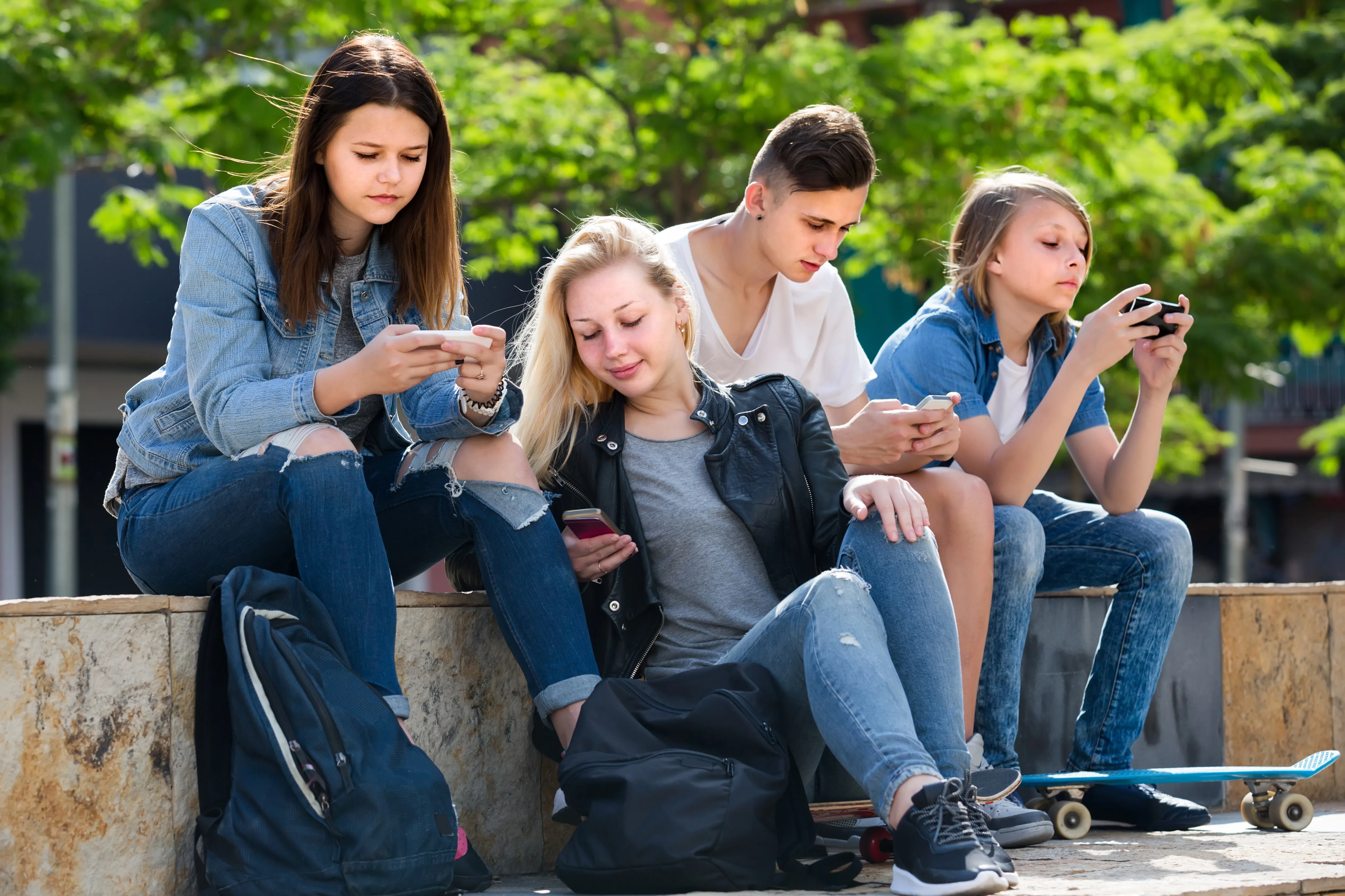 Jongeren zitten op een muurtje op hun telefoon