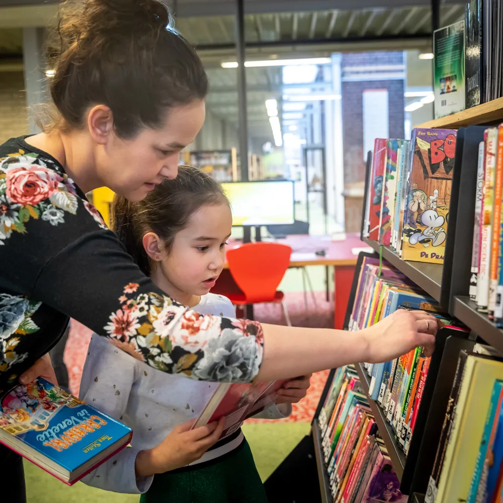 Moeder en kind zoeken boeken in kast