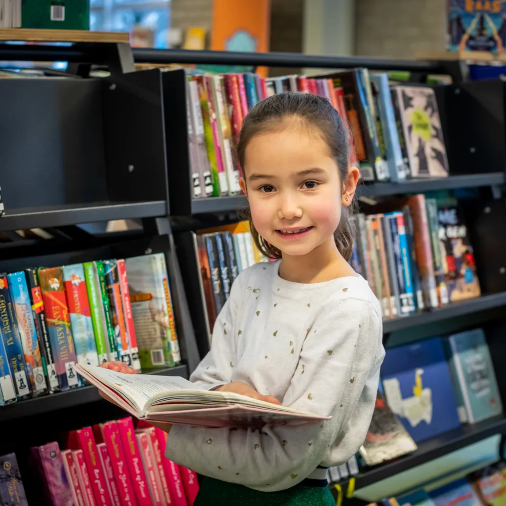 Meisje met open boek bij boekenkast