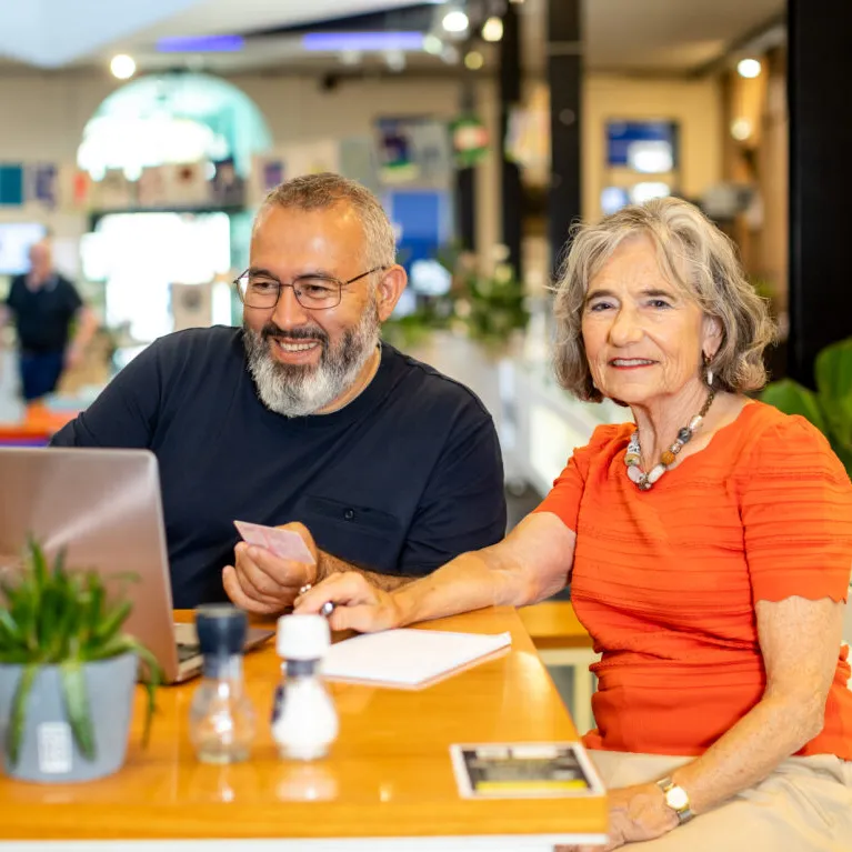 Een man en een vrouw zitten samen lachend achter een laptop.