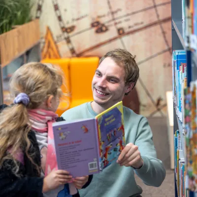 Lachende man en meisje in schoolbieb met boek in hand