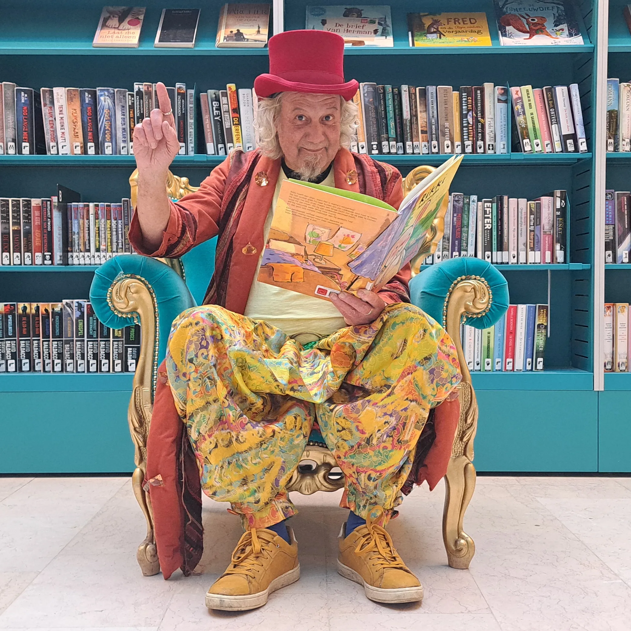 De verhalenverteller zit op een voorleesstoel in de bibliotheek van Sint-Michielsgestel in kleurrijke kleding