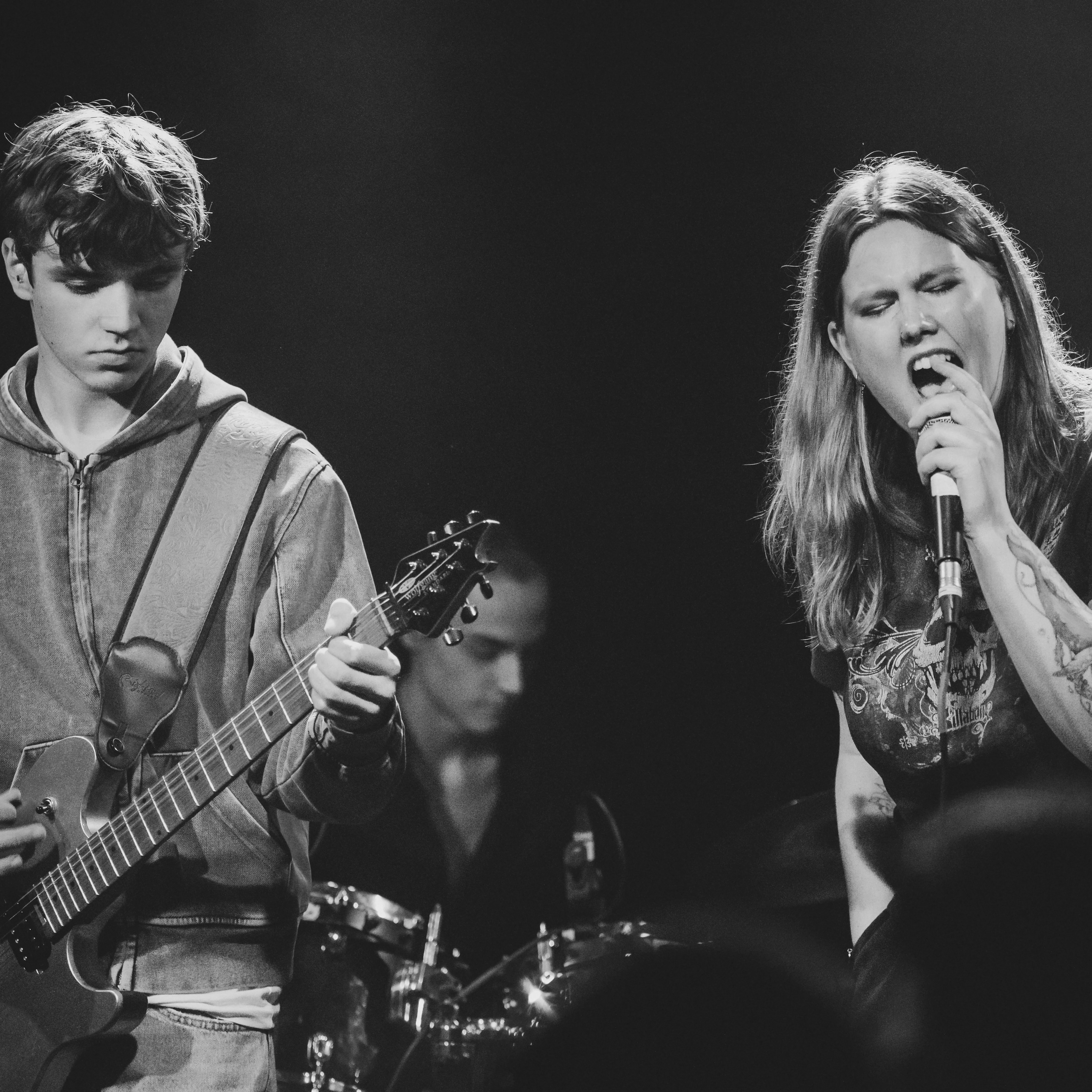 meisje die zingt, jongen op gitaar, jongen op drums, zwart wit foto, bandje