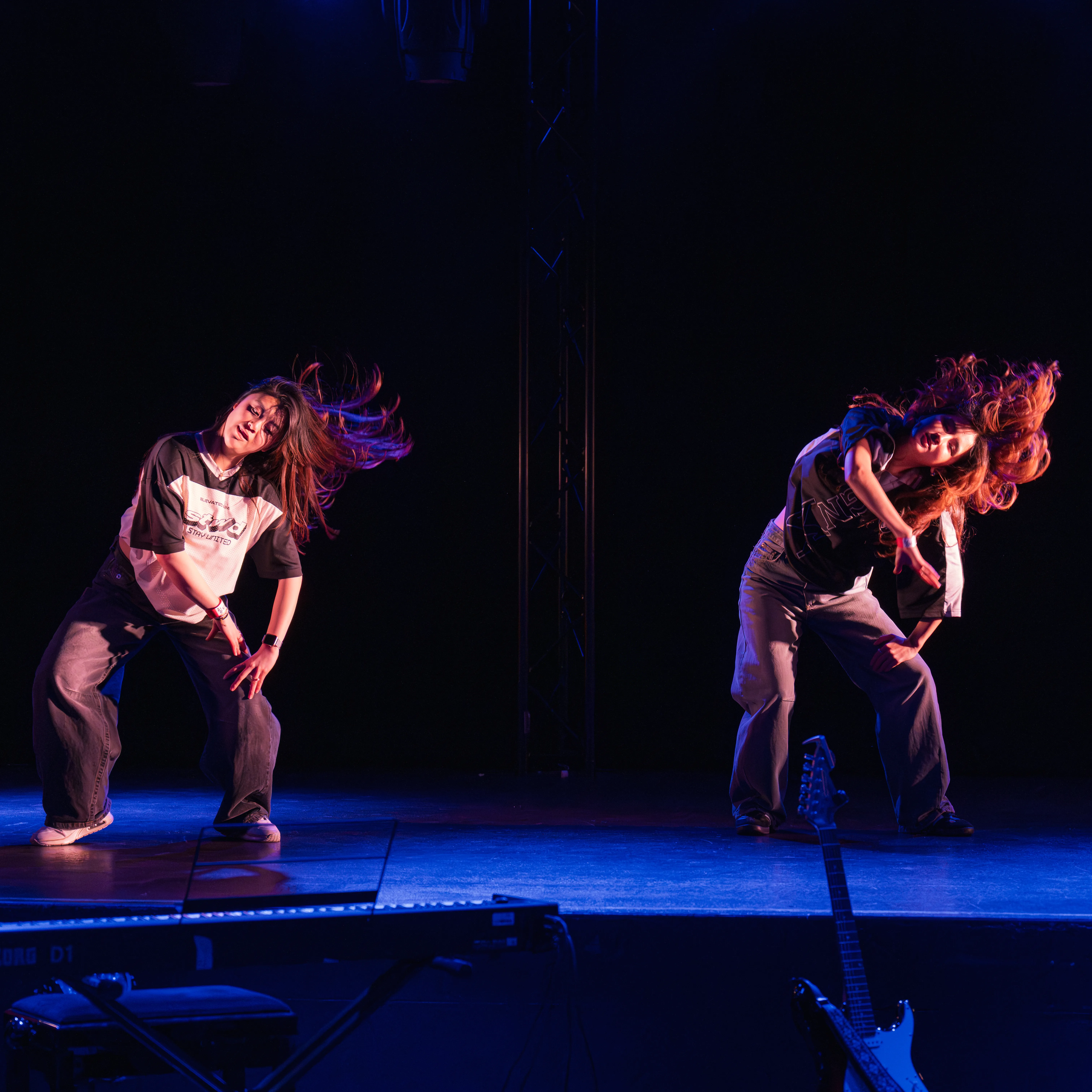 twee jonge vrouwen op een podium aan het dansen, hun haar zwiert alle kanten op 