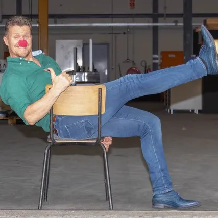 Man op een stoel met een rode clownsneus