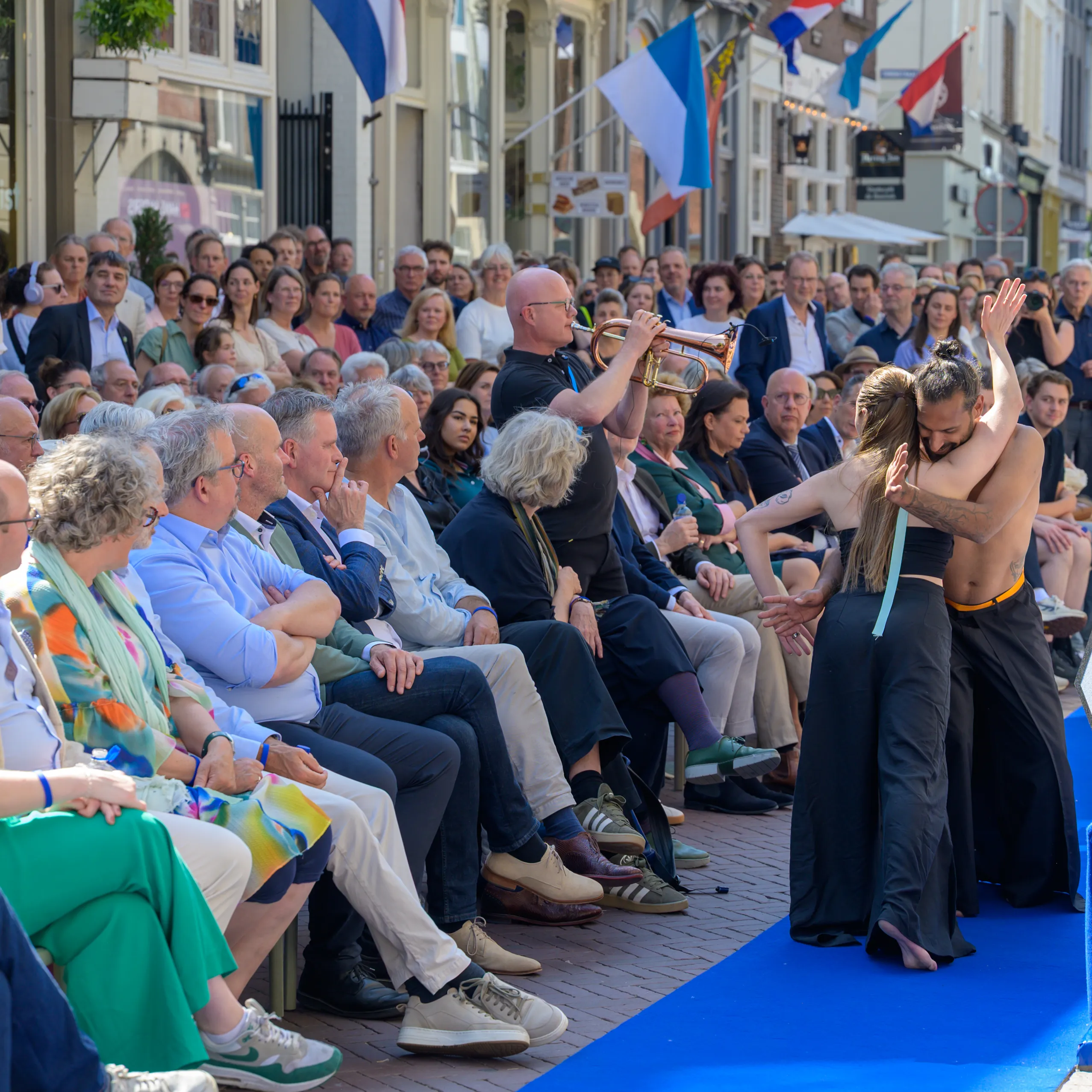 publiek kijkt geboeid naar twee dansers op blawe loper buiten