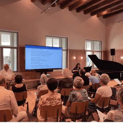 Publiek in zaal met scherm en piano 