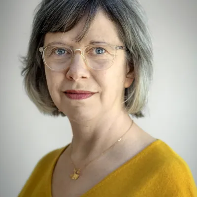 Portret van vrouw van middelbare leeftijd met grijze bob, bril en gele trui