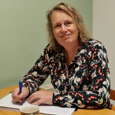 Foto vrouw met lichtbruin haar die achter een bureau zit en schrijft