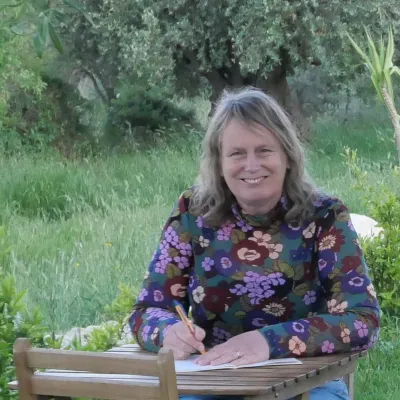 Vrouw zit aan een houten tafeltje te schrijven in de buitenlucht