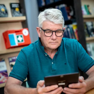 Man met grijs haar, bril en blauwe polo kijkt naar zijn tablet