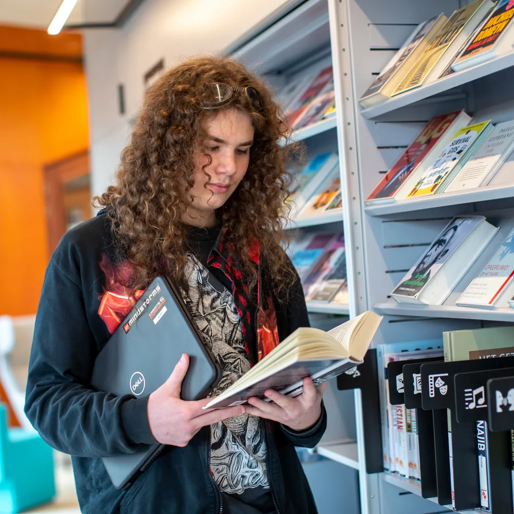 jongen met laptop bij boekenkast
